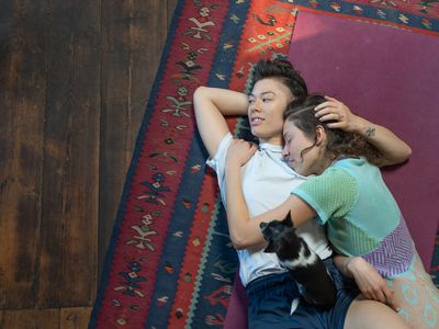 A lesbian couple lying on a rug on the floor and embracing each other affectionately.