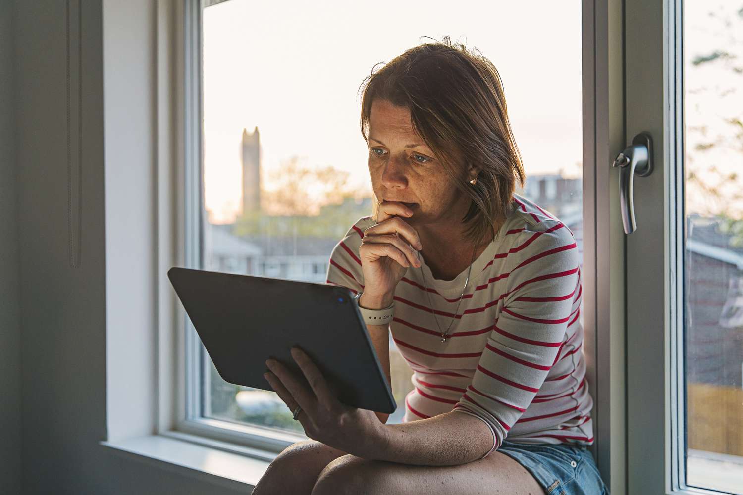 Woman using digital tablet on window sill